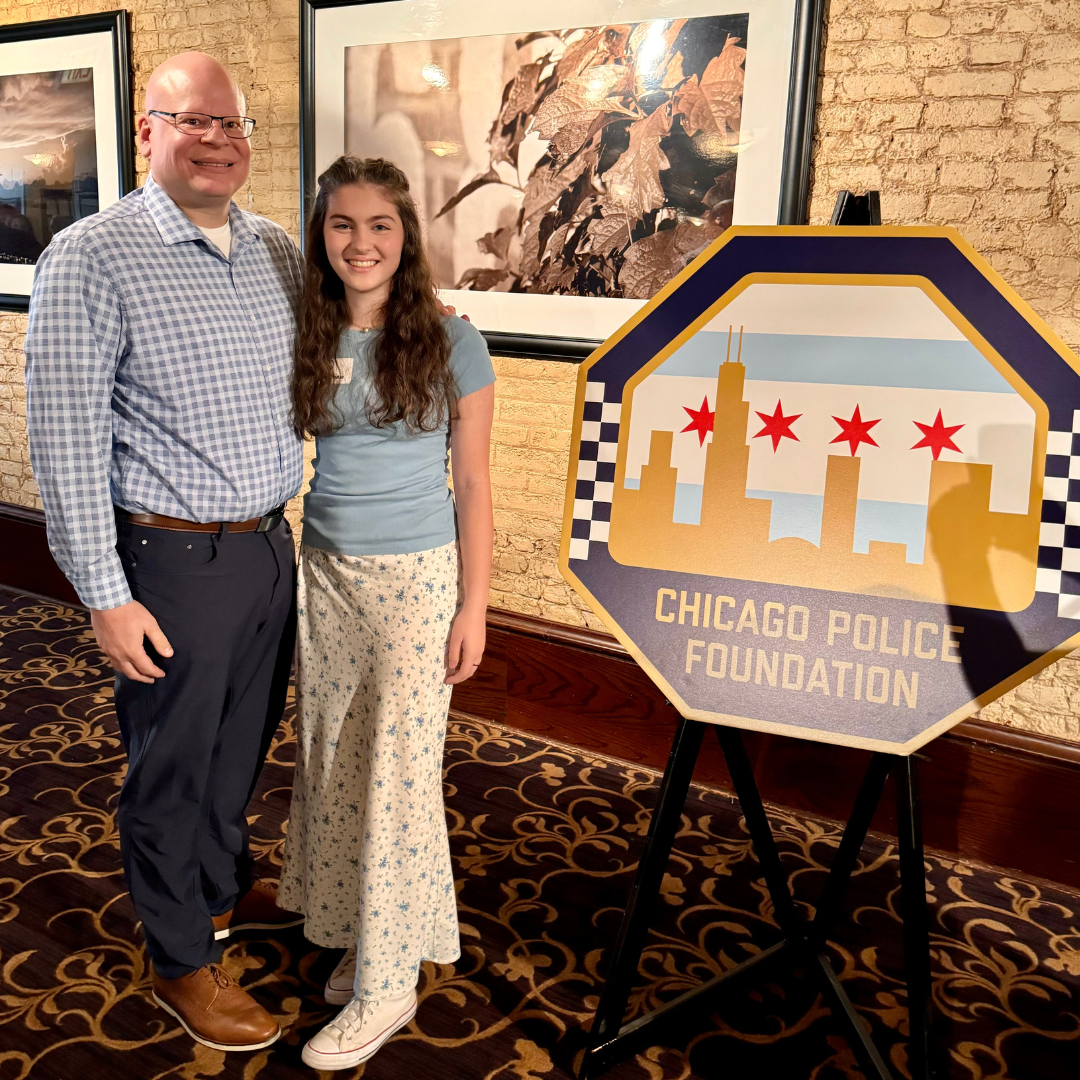 Chicago Police Officer Jay Padar standing next to his daughter Maddie, both smiling, next to a Chicago Police Foundation sign